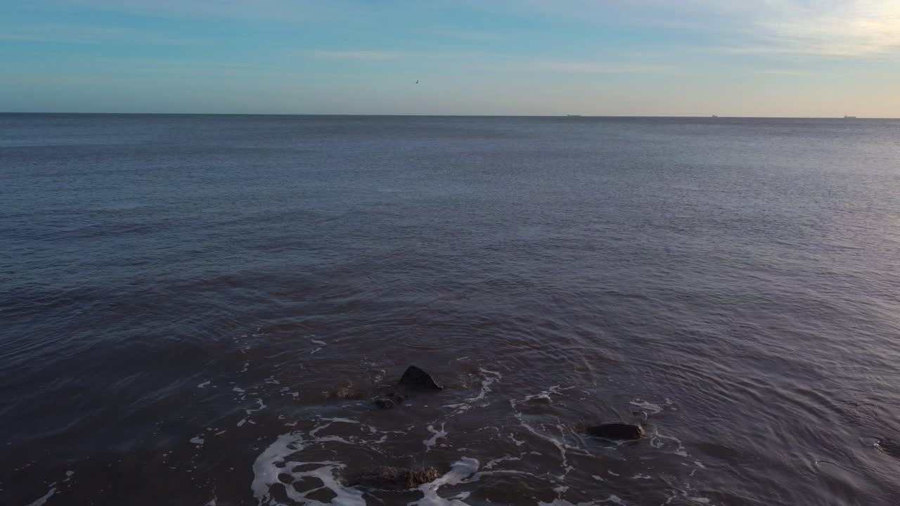 Person Standing on Rocky Shore at Sunset
