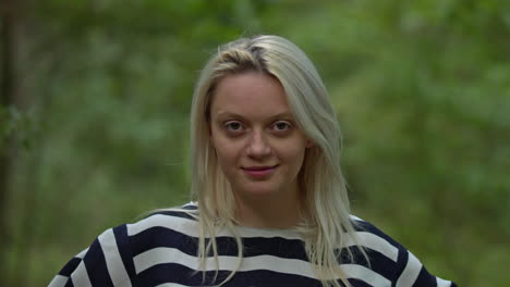 Portrait-of-pretty-happy-blond-woman-smiling-to-camera-on-green-park-background