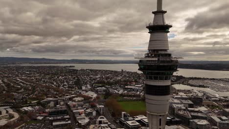 aerial orbit of sky tower with marina port and cityscape of auckland city, new zealand. wide shot. cloudy day in summer. suburb neighborhood in distance