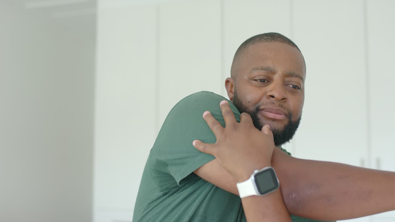 African American man feeling shoulder pain, rubbing shoulder in room, in green tee and white watch