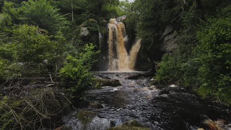 Slow-moving-drone-shot-towards-a-rare-powerful-Yorkshire-Waterfall-surrounded-by-trees-in-autumn