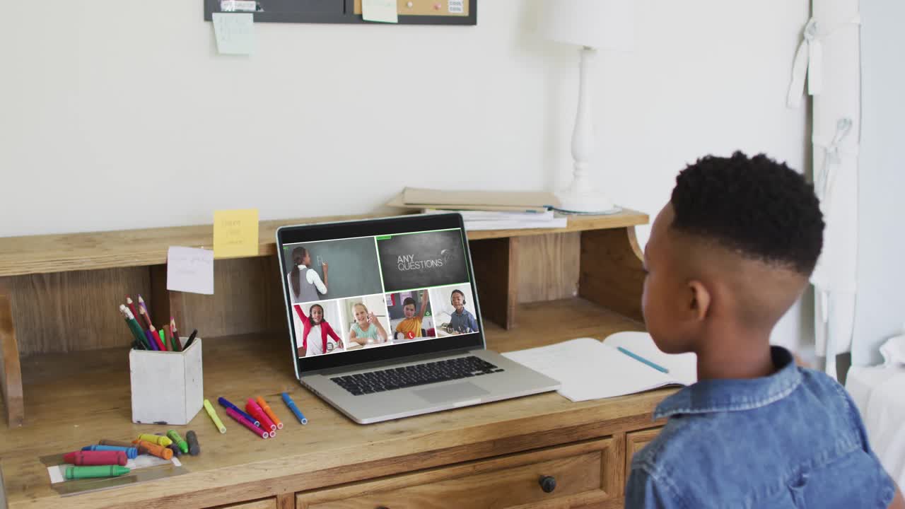Menino afro-americano levantando as mãos enquanto faz uma videoconferência no laptop em casa.
