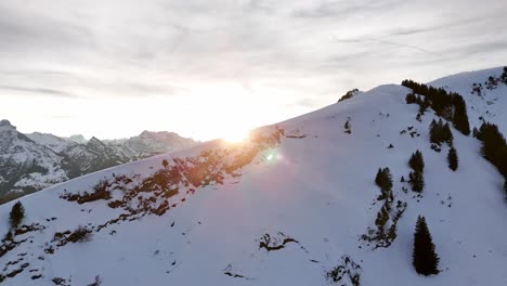 Aerial-flyover-snowy-slope-of-swiss-mountain-and-magnificent-mountain-range-panorama-with-golden-sunset-in-Background