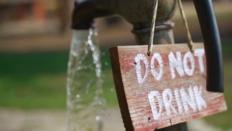 "do not drink" sign hangs on the back of an old iron faucet pouring water out on a summer day