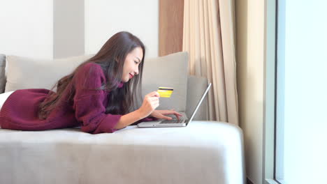 shopping online from sofa, young happy asian woman buying stuff on internet using credit card and laptop, full frame