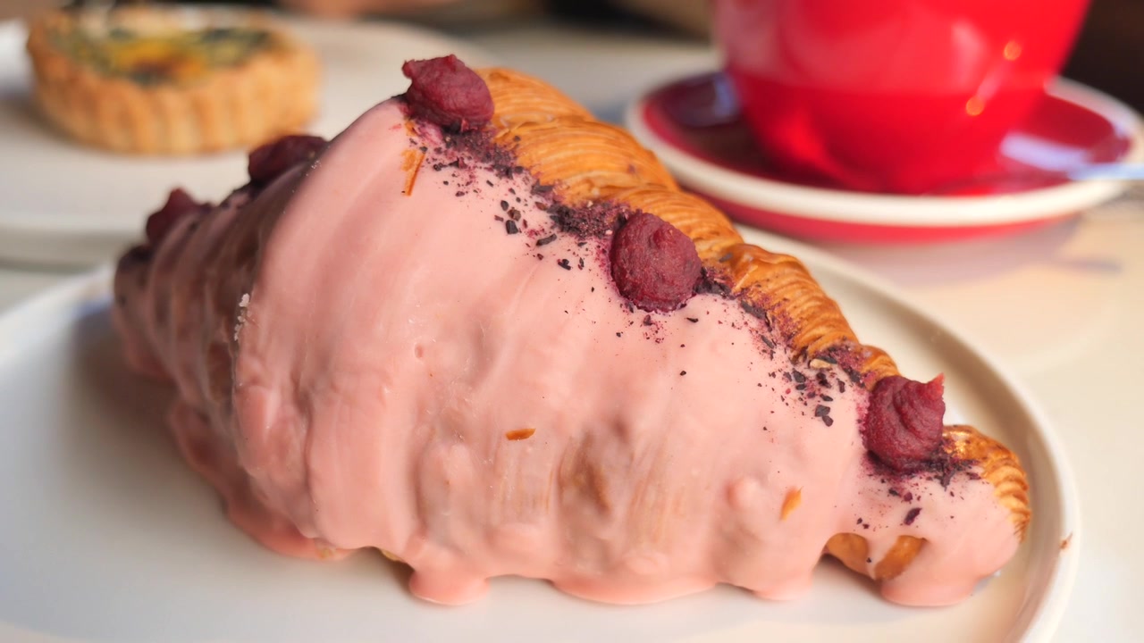 Cornetto glassato rosa con frutti di bosco su un piatto.