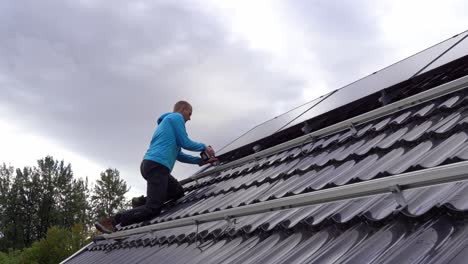 technician fastening solar panels on rooftop during installation process - static with male worker installing panels on private home and cloudy sky background