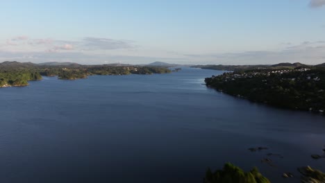 Aerial-hyperlapse-over-smooth-Norwegian-water-snaking-up-across-green-forested-islands-on-coast-with-homes