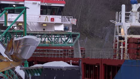 dumper arriving and emptying his bucket of anorthosite minerals for loading into ships cargo hold - dumper in front with conveyor belt in middle and ship in background - gudvangen norway static