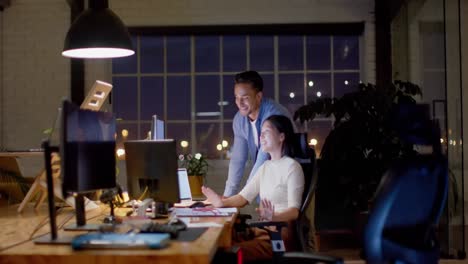 happy diverse male and female colleague talking and using computers at night in office