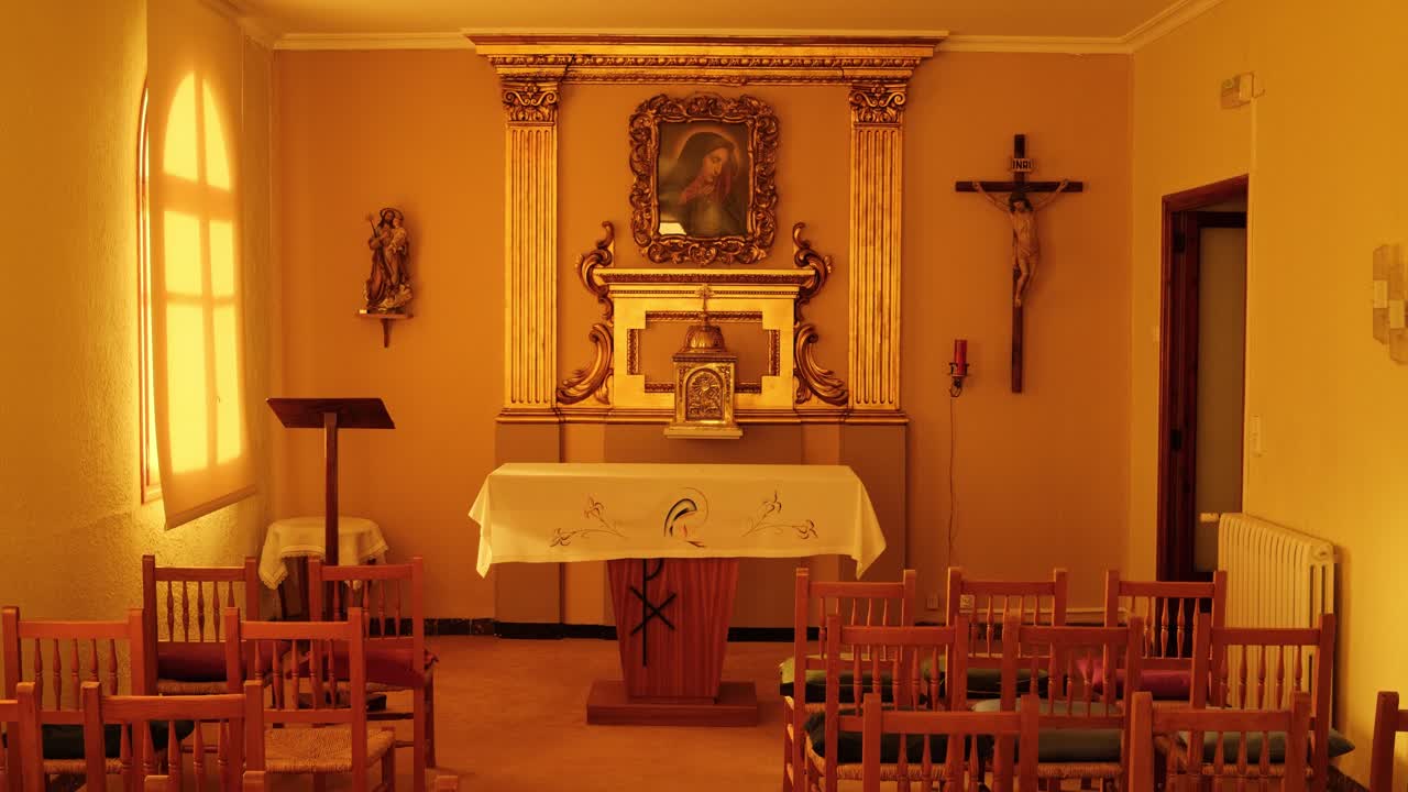 Una cappella vuota illuminata da luce calda con sedie rivolte verso un altare e arte religiosa sulle pareti