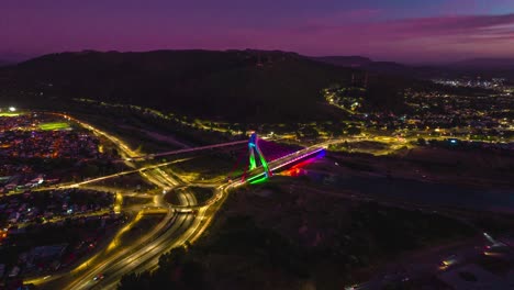 Lufthyperlapse-über-Der-Stadt-Temuco-Bei-Sonnenuntergang-In-Der-Nacht-In-Chile,-Kreisverkehr,-Kabelbrücke-über-Dem-Fluss-Cautin,-Hügelhäuser-Im-Andental-Der-Region-Araukarien