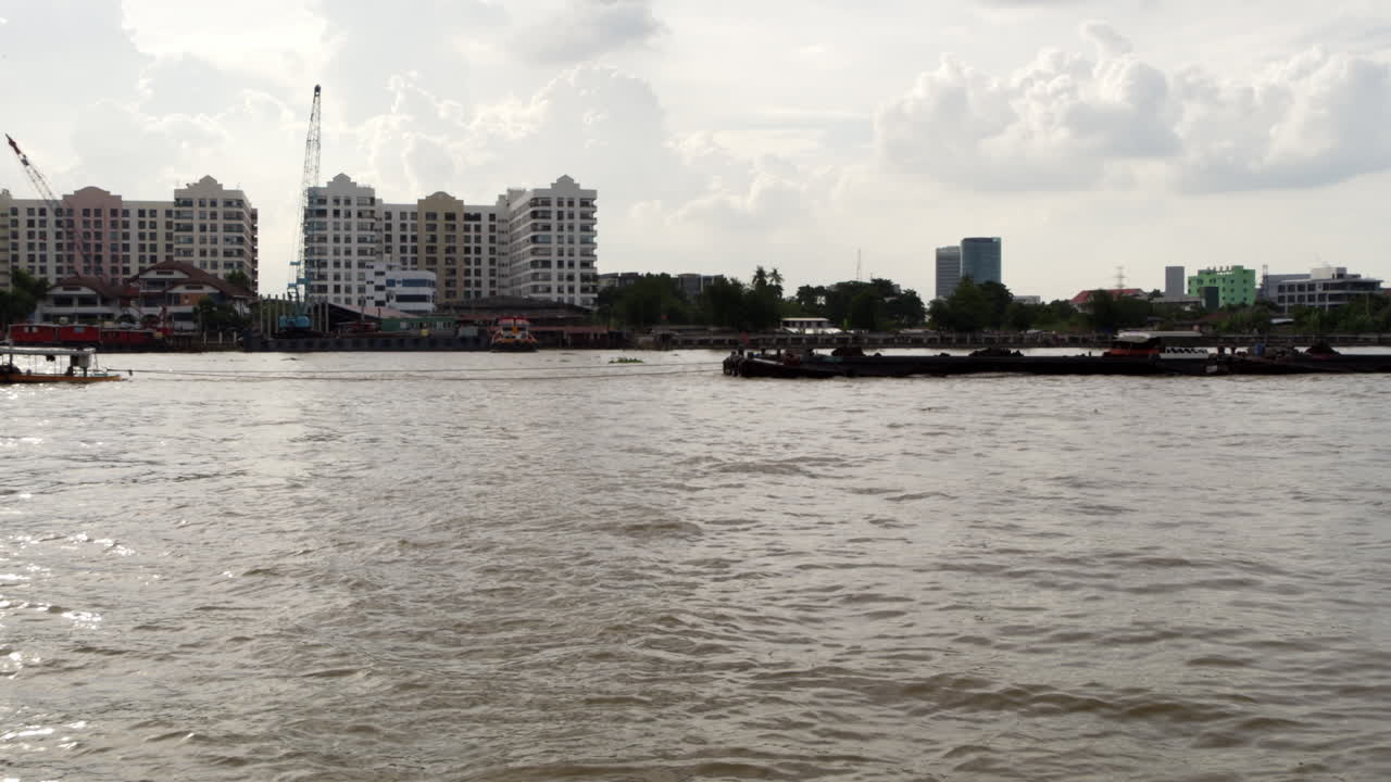 A tugboat drags a sand-loaded cargo ship along the Chao Phraya River, illustrating waterway transport and freight delivery.