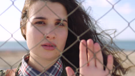 sad young woman standing trapped behind a wire