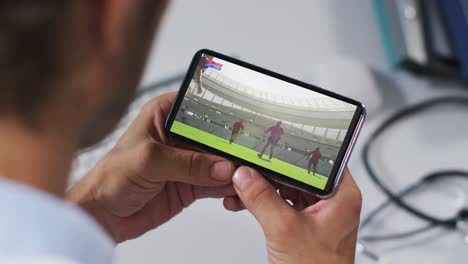 Compuesto-De-Un-Médico-Masculino-Viendo-Un-Partido-De-Rugby-En-Un-Teléfono-Inteligente