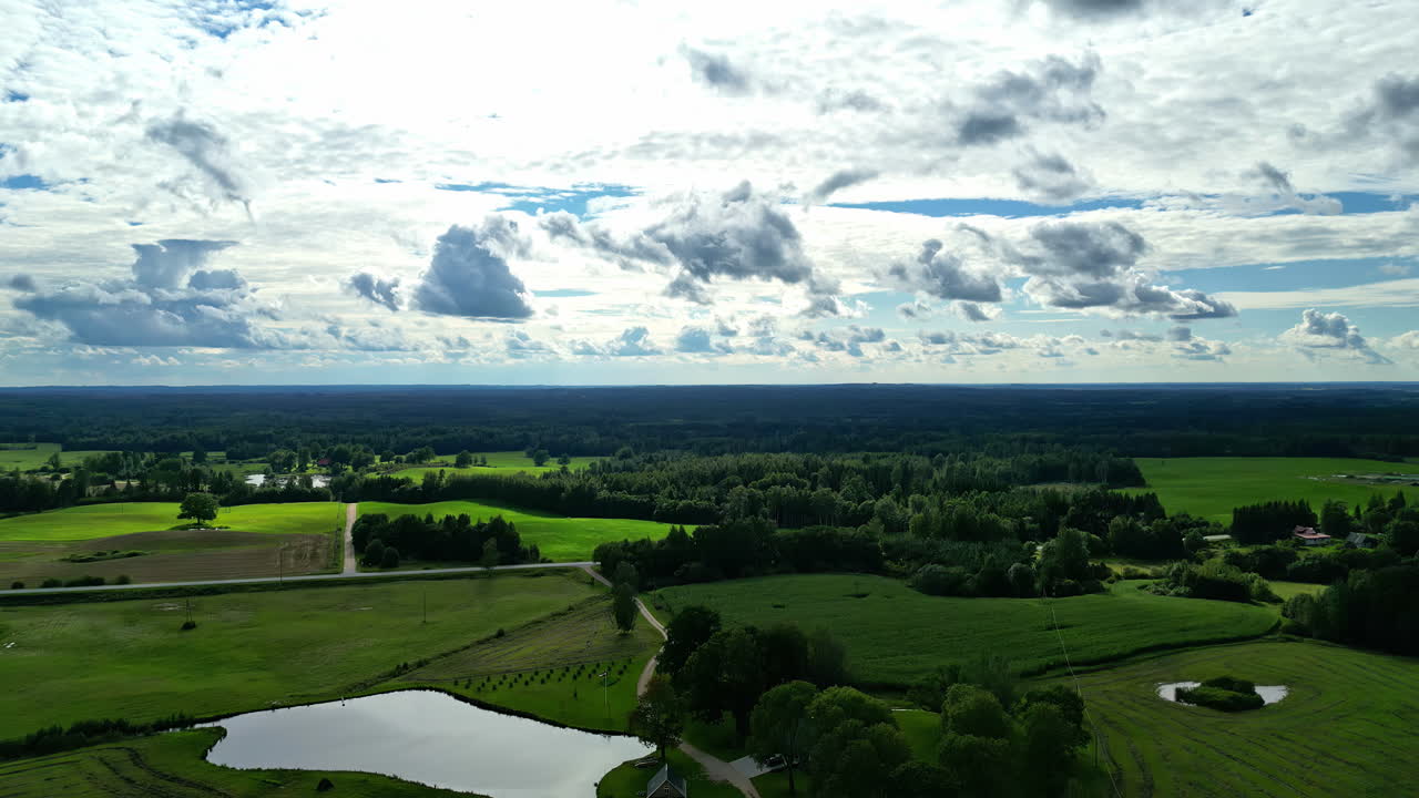 Aerial view of cumulus clouds on sky with rural green field filled with lush trees and bushes during morning.