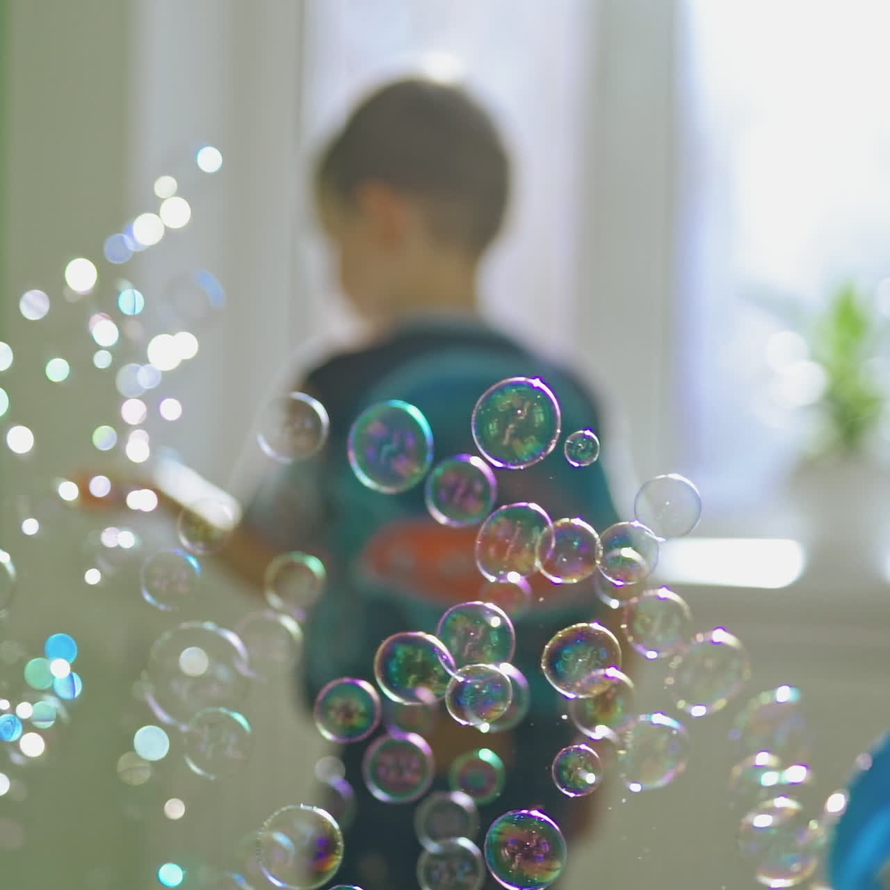 Many aqua bubbles flying in the room on blurred background with a little boy. Cute child having fun with soap bubbles indoors.