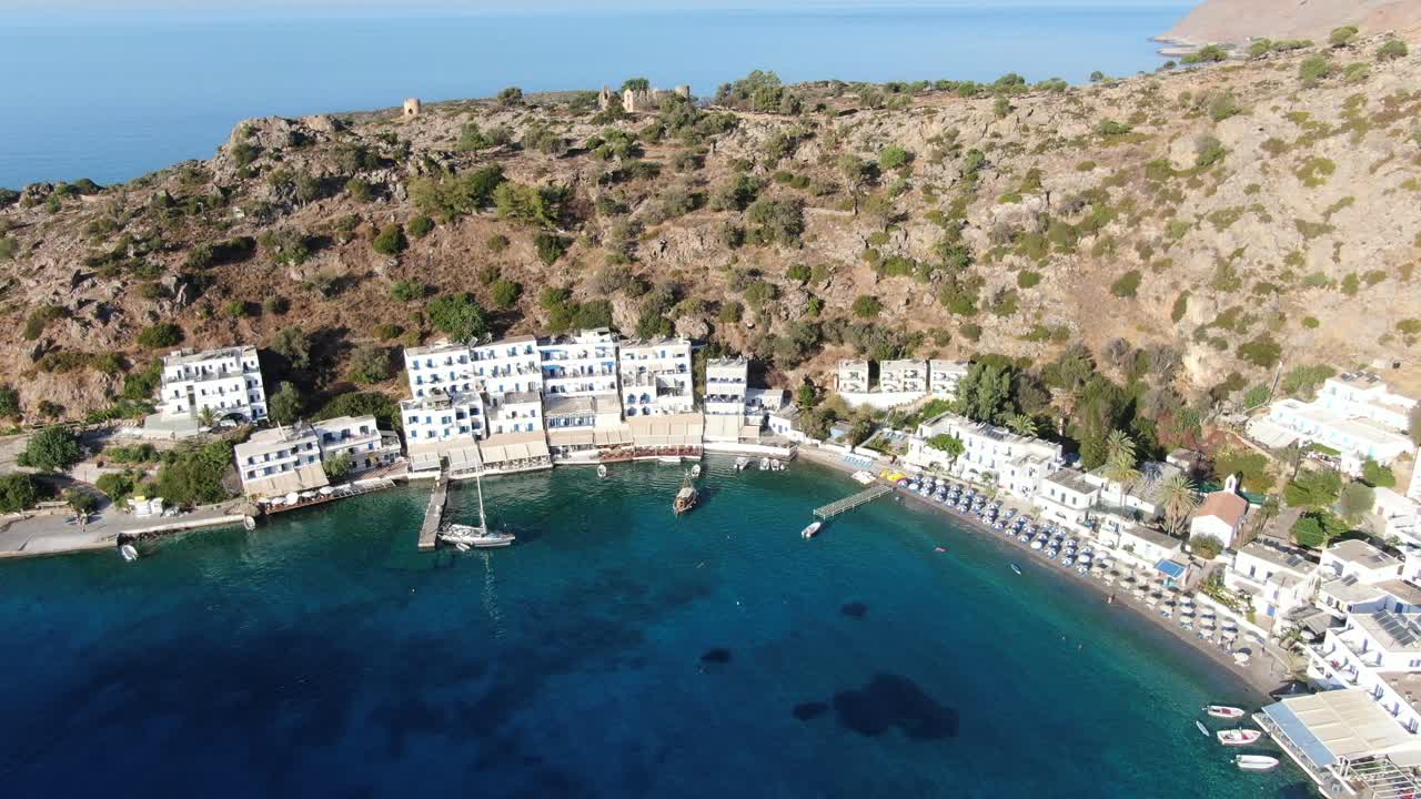 vista de drones en grecia volando sobre el mar azul en loutro pequeña ciudad de casas blancas y pequeños barcos al lado de una colina en un día soleado