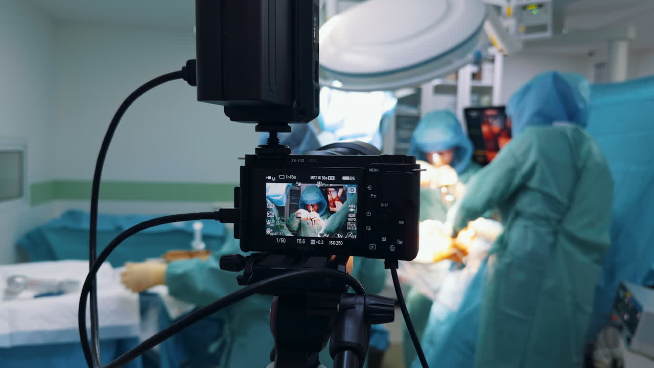 Kyiv, Ukraine, 2 August 2025: Close-up on a camera screen displaying a surgical procedure in progress. The camera on a tripod is filming the medical team working under bright dome lights in the operating room