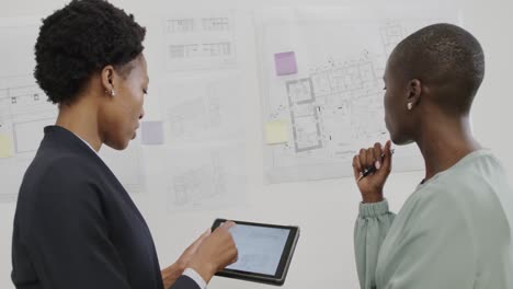 Afroamerikanische-Architektinnen-Diskutieren-In-Zeitlupe-über-Baupläne-Und-Nutzen-Tablets-Im-Büro