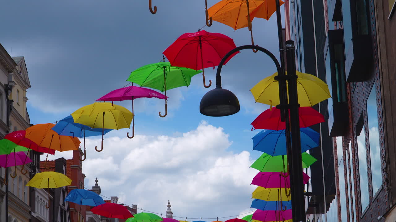 Floating colorful umbrellas hung across a city street in Gdańsk, Poland, under a bright cloudy sky