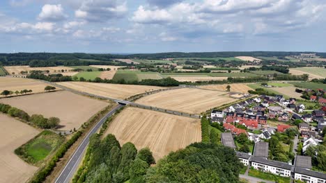 aerial establishing flight over small town of america, near agricultural farm fields and highway road. rural area with hills and cultivated wheat fields in usa. clouds at sky in summer. wide shot