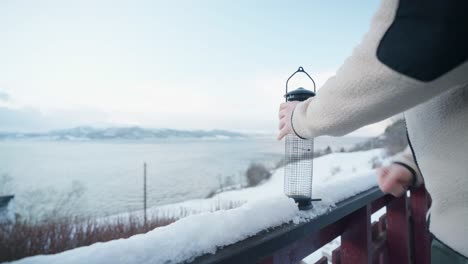 Mann-Füllt-Den-Vogelhäuschen-Mit-Samen-Auf-Schneebedeckter-Zaunschiene