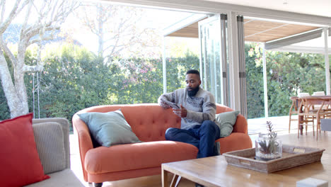 African-american-man-using-tablet-and-credit-card-in-sunny-living-room,-slow-motion