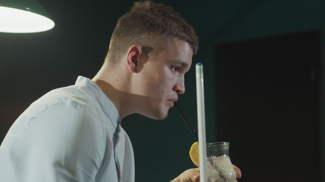 색 셔츠를 입은 신사가 이를 들고 검은 으로 레몬 음료를 마시고 있는 클로즈업 사이드. 위쪽 램프 조명은 집중된 표현을 강조하며 정교한 풀홀을 만니다.