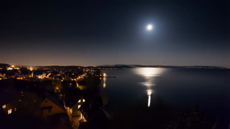 moonlight reflection on a lake with an illuminated lakeside village at night