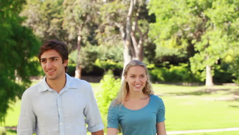 una pareja camina hacia la cámara juntos y luego ríen y saludan en ella
