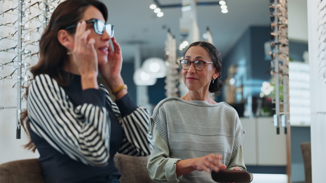 Two women are in an optometrist's office, trying on glasses and laughing