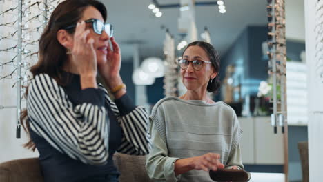 two women are in an optometrist's office, trying on glasses and laughing