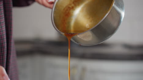 vista parcial de una persona con ropa a cuadros vertiendo sopa roja rica de una olla inoxidable mientras se agita, el líquido espeso fluye suavemente mientras el cocinero prepara una comida casera en la cocina moderna