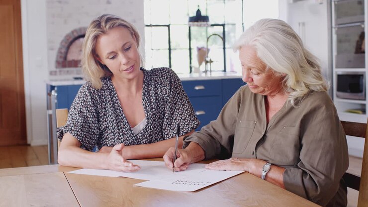 Female Friend Helping Senior Woman To Complete Last Will And Testament At Home