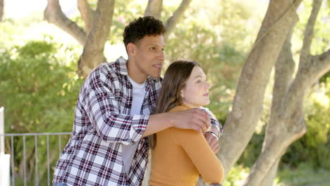 Happy-diverse-couple-standing-on-balcony-and-embracing-at-home,-in-slow-motion