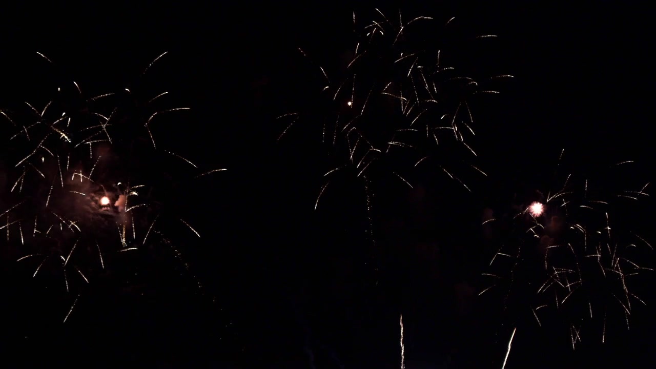 Cielo notturno nero illuminato da luci scintillanti mentre uno spettacolo pirotecnico esplode e illumina l'oscurità della sera. Spettacolo di fuochi d'artificio con razzi abbaglianti e brillanti esplosioni in alta quota
