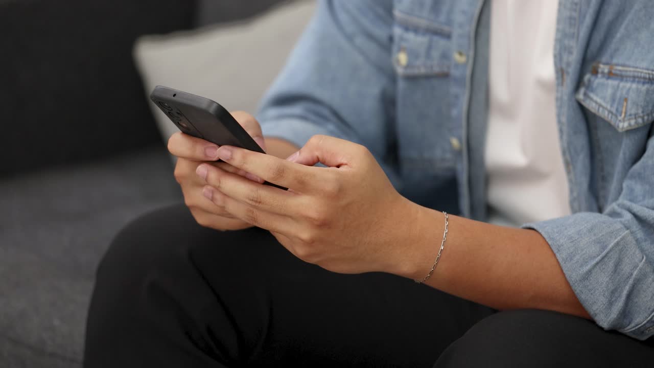 Un giovane adulto con una giacca di jeans usa uno smartphone mentre è seduto su un divano