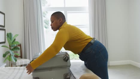 feliz afroamericana de tamaño grande mujer empacando una maleta en el dormitorio