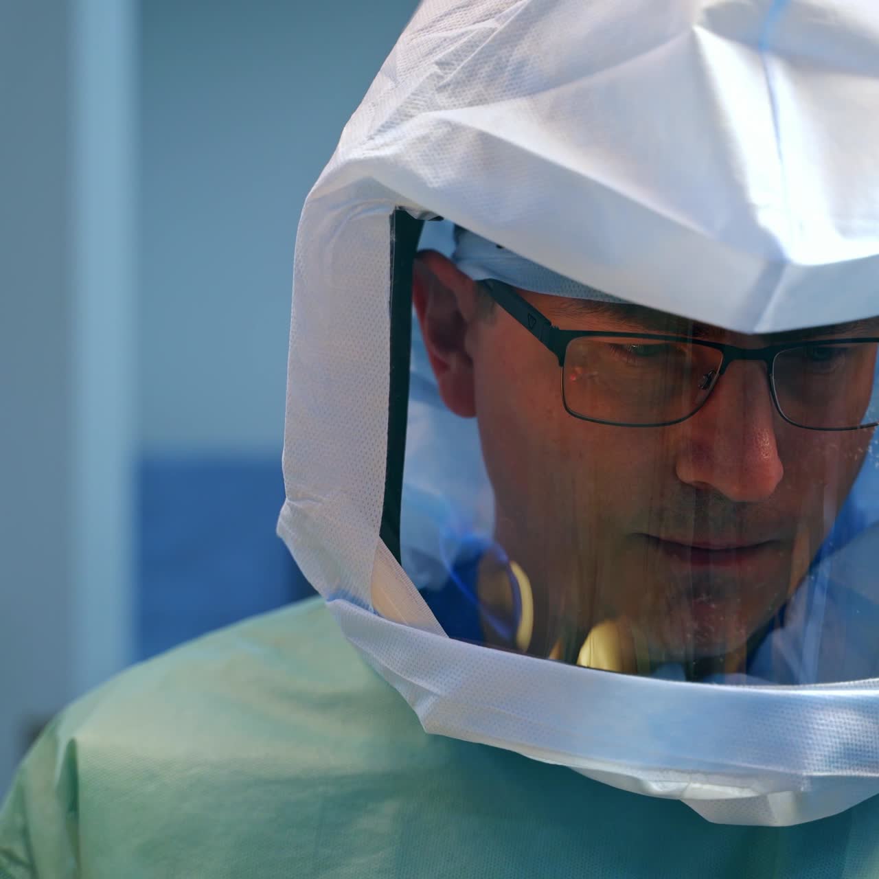 Concentrated face of a surgeon in glasses and protective suit. Close up portrait of professional at work