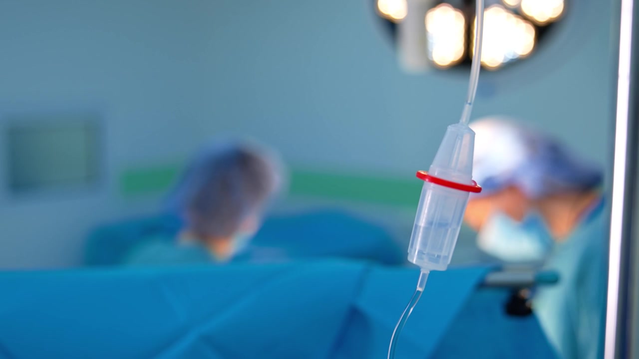 Liquido trasparente che gocciola all'interno del serbatoio del contagocce. Primo piano. Flebo in sala operatoria. Medici lavorano sullo sfondo sfocato.