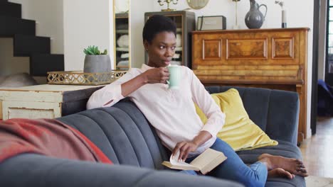 happy african american woman sitting on sofa in living room, reading book