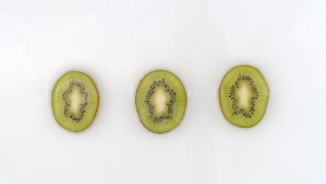 slow motion water splash on three slices of green kiwi lying on a white background in the water