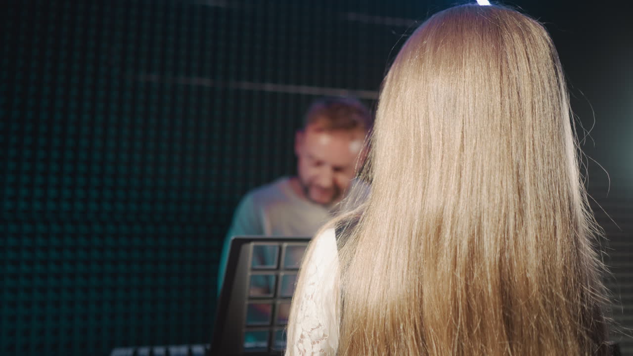 아이는 오디오 스튜디오에서 선생님과 함께 노래를 부릅니다. 금발 어린 소녀는 작곡가가 수업에서 피아노를 연주하는 동안 보컬 퍼포먼스를 연습합니다. 재능있는 아이 수업