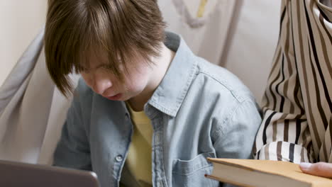 closeup of young gir with down syndrome using laptop next to woman with book