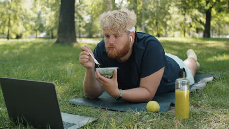 Hombre-Con-Sobrepeso-Comiendo-Ensalada-Y-Usando-Una-Laptop-En-El-Parque