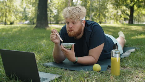 overweight man eating salad and using laptop in park