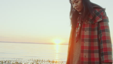 young woman with lantern walking along lake shore at sunset