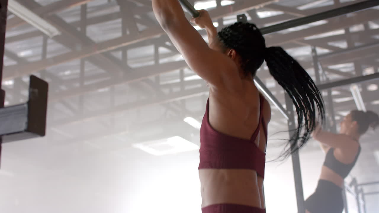 Doing pull-ups, women exercising in gym, focusing on upper body strength
