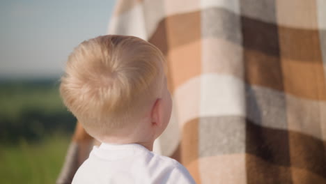 a joyful young child in a white shirt playfully hits a flowing plaid scarf in a grassy field. the child's playful energy is captured in this close-up